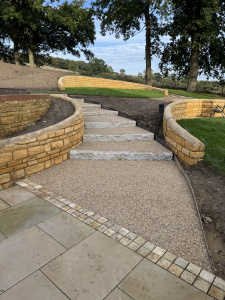 Granite kerbs, curved limestone retaining walls from cotswold quarry add movement and grandeur to this hillside garden design